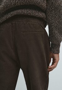 Brune pæne corduroy bukser med ribbet struktur, elastisk talje og to baglommer. Sweater synlig ovenfor med et tekstureret mønster.