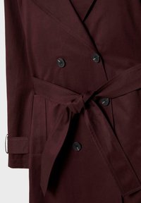 Burgundy kaksirivinen takki, jossa on vyösolki, mustat napit ja käsivarsisomistus, valmistettu sileästä kankaasta, jossa on matta pinta.