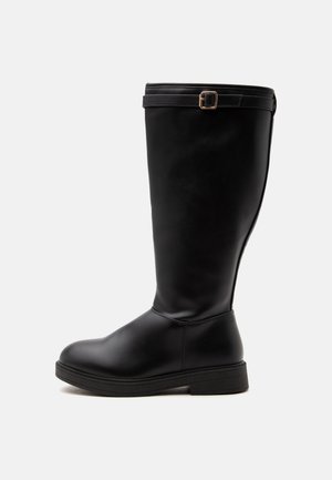 Botte en cuir noire montant jusqu'au genou avec un petit talon et une sangle réglable avec boucle dorée près du haut, vue de côté sur fond blanc.