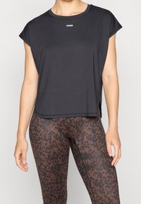 Svart träningslinne med korta ärmar, rund hals och lös passform. Matchas med bruna leggings i leopardmönster med texturerade detaljer.