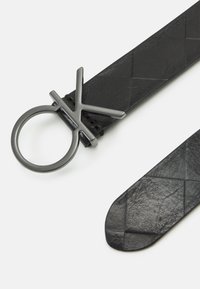 Cintura in pelle nera con una texture intrecciata e una fibbia metallica circolare con un design angolare. Le estremità sono affusolate per una chiusura sicura.