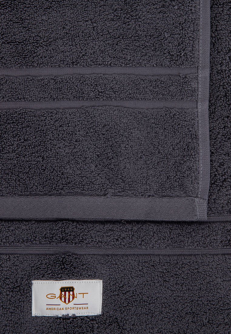 Dunkelgraues Handtuch aus strukturiertem, schlingenförmigem Gewebe. Verfügt über ein weißes Etikett mit orangefarbener und schwarzer Markenkennzeichnung an der Unterseite. Vertikale und horizontale Streifen sind sichtbar.