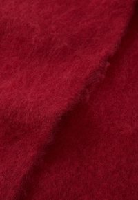 Tissu rouge, texturé, avec une surface douce et duveteuse. Le matériau semble épais et chaud, présentant une couleur riche et uniforme sur toute sa surface.