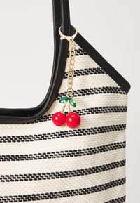 Borsa a spalla a righe in materiale intrecciato nero e crema; presenta un bordo in finta pelle nera e un ciondolo a forma di ciliegia rossa con foglie verdi.
