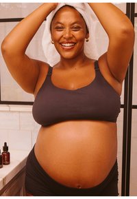 Schwarzer Still-Bralette mit verstellbaren Trägern, kombiniert mit schwarzen Shorts. Person mit einem Handtuch auf dem Kopf steht in einem gut beleuchteten Badezimmer.