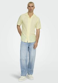 Lichtgele kortärmedige overhemden met knoopsluiting en een kraag, gecombineerd met lichtblauwe wijde jeans en witte sneakers.