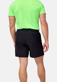 Svarta atletiska shorts med en åtsittande midja, med en bakficka med dragkedja och en slät textur. Bärs med en ljusgrön kortärmad skjorta.