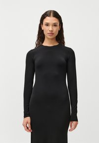 Vestido preto de mangas longas, feito de um tecido suave e elástico. Silhueta ajustada com um decote redondo e costuras mínimas. Design simples, sem padrões.
