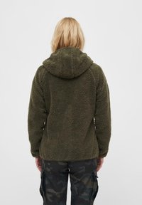 Olivgrön fleecejacka med huva, som har ett mjukt, texturerat tyg och en avslappnad passform, kombinerad med camouflage-mönstrade cargobyxor.