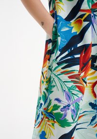 Blumenminikleid mit einer Vielzahl von lebendigen Farben, leichtem Stoff und einer seitlichen Taschenveredelung. Die Muster umfassen tropisches Laub und Blumen.