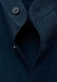 Navy blue linen shirt collar with a button. Features a smooth texture and clean stitching along edges, showcasing a simple design.