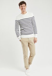 Maglione a righe blu navy e bianche con scollatura rotonda e dettagli con bottoni; chino beige; sneaker bianche; vestibilità rilassata, texture liscia.