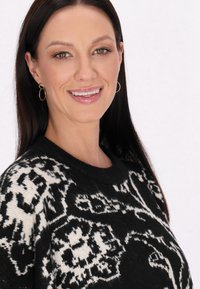 Pulover cu model alb și negru, cu guler rotund și o textură moale, având un design spiralat și manșete cu nervuri. Cercei cu cercuri aurii.