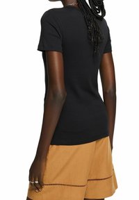 Zwarte katoenen t-shirt met korte mouwen, een gladde textuur en een fitted ontwerp, gecombineerd met lichtbruine shorts met decoratieve uitsparingen.