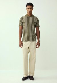 Groene en witte gestreepte polo met korte mouwen, kraag en een rechte pasvorm, gecombineerd met lichtbeige broek en bruine schoenen.