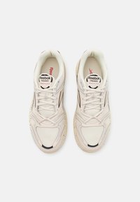Ett par krämfärgade Reebok Premier Road Plus VI sneakers med vita snören och svarta detaljer, visade ovanifrån på vit bakgrund.