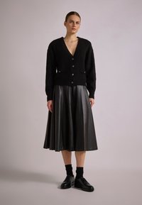Black knitted cardigan with a deep V-neck and buttons, paired with a black leather midi skirt. The ensemble features a smooth texture and tailored fit.