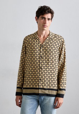Langärmliges Hemd in Beige und Schwarz mit geometrischem Muster, einem eingeschnittenen Kragen und Knopfverschlüssen, kombiniert mit hellblauen Jeans.