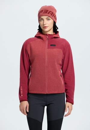 Rode fleecjacket met een capuchon, gestructureerd lichaam, gladde mouwen, voorzak met rits en roze accenten. Gecombineerd met zwarte leggings.