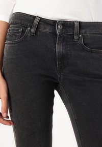 Jeans de mezclilla negra con corte ajustado, que cuentan con un diseño de cinco bolsillos, cierre de botón metálico y un ligero desgastado para un aspecto usado.