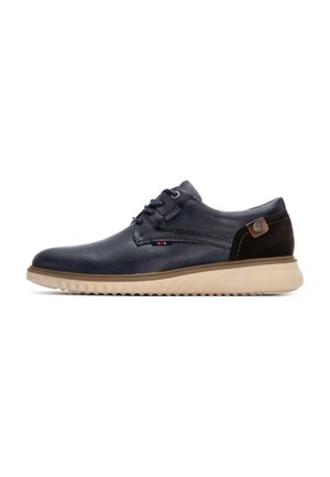 Zapato de cuero marino con un acabado suave, diseño de cordones y suela de goma beige. Presenta un detalle de gamuza marrón y logotipo en el costado.