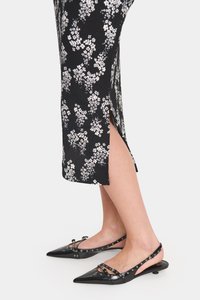Fekete virágmintás midi ruha texturált felülettel és oldalsó hasítékkal, fekete műanyag ponthegyes hátpántos cipőkkel párosítva, díszítő szegecsekkel.