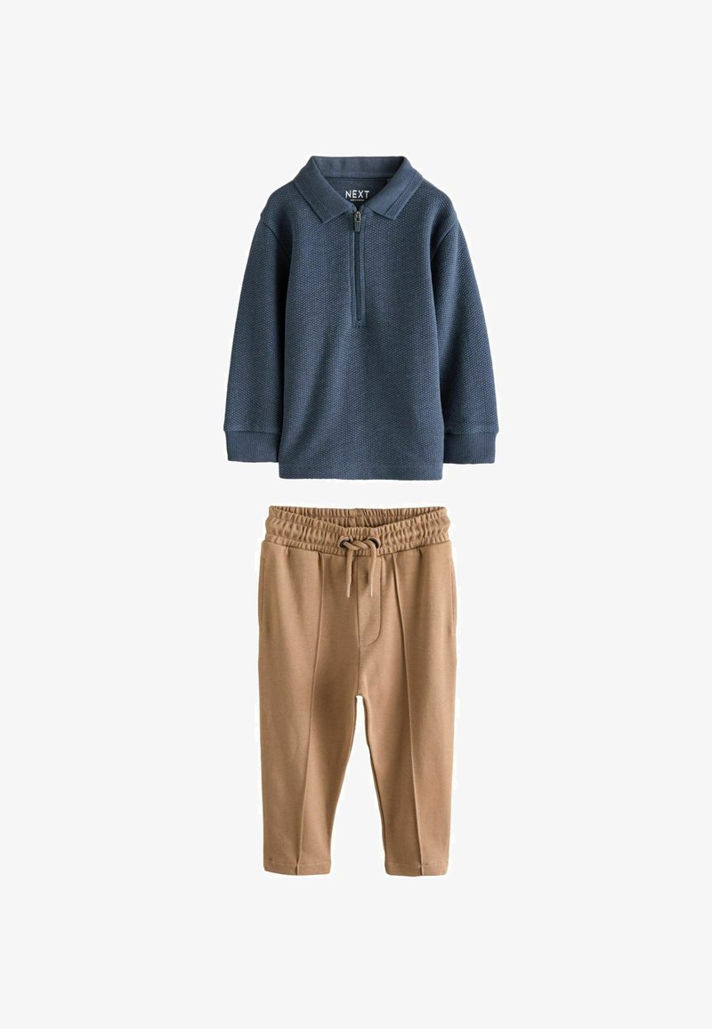 Dvojdielny outfit pozostávajúci z modrého polokošele s dlhým rukávom a polovičným zipsom a khaki elastických nohavíc s viazaním v páse.