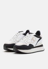 Baskets à plateforme blanches et noires avec fermeture à lacets, détails cloutés formant un motif sur les côtés, et semelles en caoutchouc texturées.