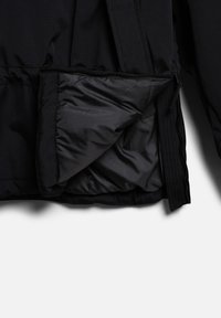 Veste noire partiellement dézippée montrant une doublure intérieure lisse et matelassée ainsi que la texture du tissu extérieur sur un fond blanc.