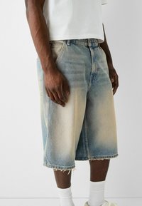 Shorts vaqueros de corte relajado, en un tono azul desgastado y con dobladillo deshilachado. La tela presenta una textura con sutiles variaciones de color.