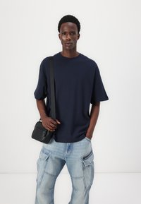 Ναυτικό μπλε oversized t-shirt κατασκευασμένο από μαλακό ύφασμα, σε συνδυασμό με ανοιχτό μπλε cargo παντελόνι που διαθέτει πολλαπλές τσέπες. Μαύρη τσάντα crossbody.