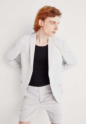 Blazer gri deschis cu o textură subtilă, două nasturi, asortat cu pantaloni scurți suflecați. Top negru ajustat dedesubt.