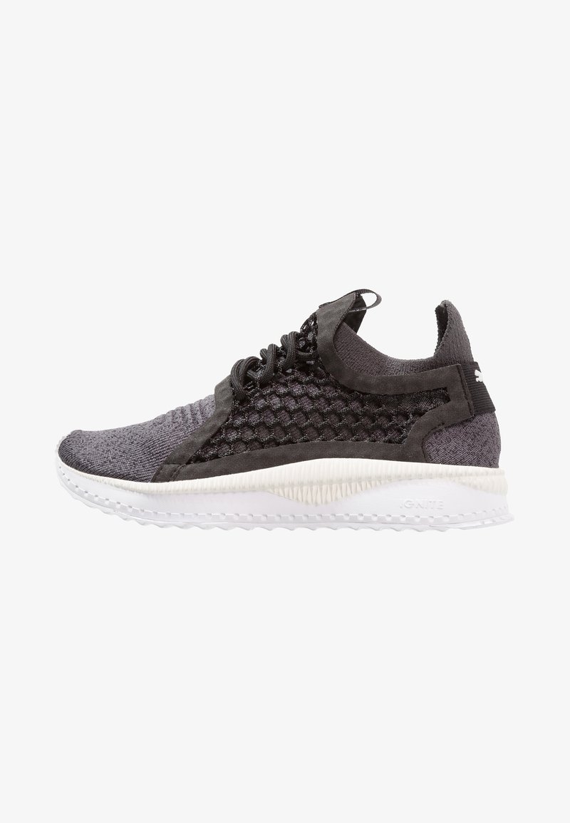 Chaussure de sport en maille noire et grise avec côtés en mesh nid d’abeille, semelle blanche texturée et languette au talon.