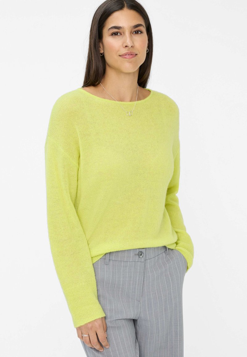 Helles limonengrünes Strickpullover mit langen Ärmeln, einem weiten Ausschnitt und einem lässigen Schnitt, kombiniert mit hellgrauen Nadelstreifen-Hosen.