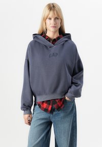 Afskåret, oversized navy hoodie med "GAP" logo i sort. Båret over en rød og sort ternet skjorte. Blødt stof og afslappet pasform.