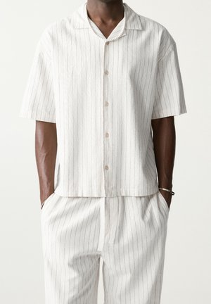 Chemise à manches courtes boutonnée en tissu léger, avec des rayures verticales grises et blanches. Coupe droite, coupe décontractée et col classique.