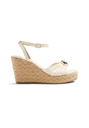 Sandalo con zeppa beige con suola in juta intrecciata, cinturino alla caviglia con fibbia, parte superiore in tessuto e ornamento rotondo metallico nella zona delle dita.