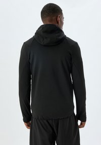 Giacca nera aderente con cappuccio, maniche lunghe e superficie liscia, caratterizzata da un design senza cuciture e uno stile minimalista.