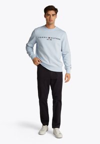 Felpa azzurro chiaro con logo nero "TOMMY HILFIGER", collo rotondo, polsini e orlo a coste, abbinata a pantaloni scuri e sneaker bianche.