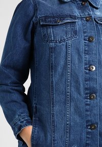 Jeansjacka i mörkblå tvätt, med två framfickor, knappstängning och strukturerad tyg. Skuren passform med långa ärmar.