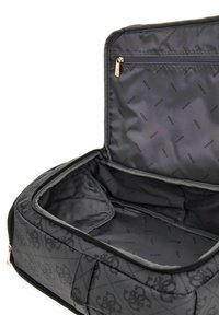 Sac de voyage noir avec un design matelassé présentant un motif de logo subtil. L'intérieur est doublé de tissu sombre et comprend une poche zippée.