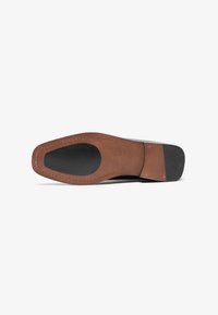 Suela de zapato de cuero con una base de cuero marrón, zona de tracción de goma negra y costura visible. Textura suave con un diseño clásico.