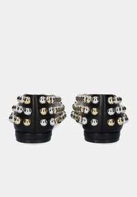 Zapatos negros adornados con tachuelas metálicas doradas y plateadas, con un diseño elegante y punta redondeada, que presentan una superficie texturizada y un tacón bajo.