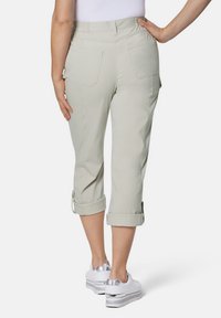 Helle beige Capri-Hosen mit einer glatten Textur, ausgestattet mit umgeschlagenen Säumen und zwei Gesäßtaschen, kombiniert mit weißen Sportschuhen.