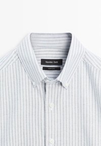 Niebiesko-biała koszula w paski z kołnierzykiem na guziki, wykonana z bawełny, z białymi guzikami i widoczną metką marki wewnątrz kołnierza.