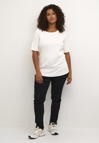 White ribbed t-shirt with short sleeves, round neckline; paired with black slim-fit pants and light-colored athletic shoes.