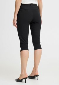 Schwarze Capri-Hosen mit körperbetontem Schnitt, ausgestattet mit einer verkürzten Länge und seitlichen Schlitzen am Saum. Hergestellt aus dehnbarem Material mit Hintertaschen.