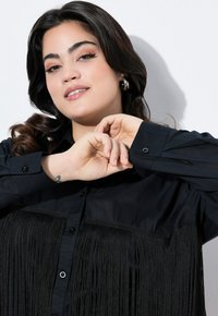 Schwarzes Button-Up-Hemd mit einem Fransen-Design auf der Vorderseite. Hergestellt aus einem glatten Stoff mit glänzenden Akzenten und präsentiert eine taillierte Passform.