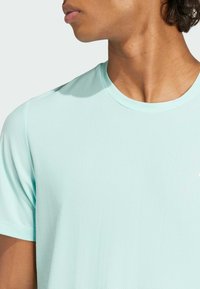 T-shirt vert menthe à manches courtes en tissu texturé et respirant. Doté d'un col rond et d'un logo de marque visible sur la poitrine.