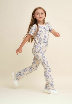 Blomstret beige ribbet to-dels sæt med korte ærmer og tætsiddende bukser. Hvide sneakers afslutter looket.
